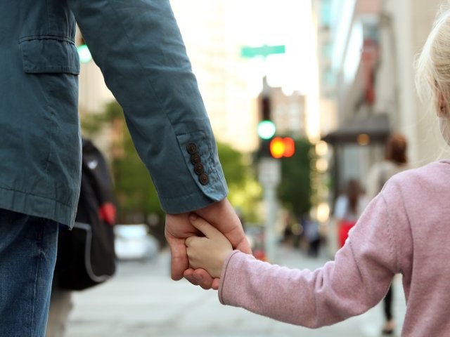 father holding the daughter/ child hand behind the traffic lights